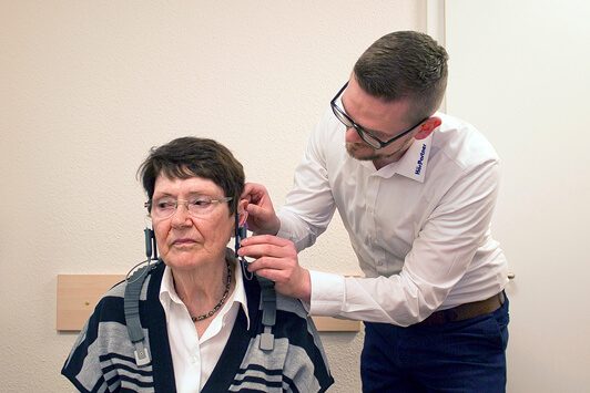 Ein Hörakustiker passt einer Seniorin ein Hörgerät bei einem Hörtest im Fachgeschäft an.