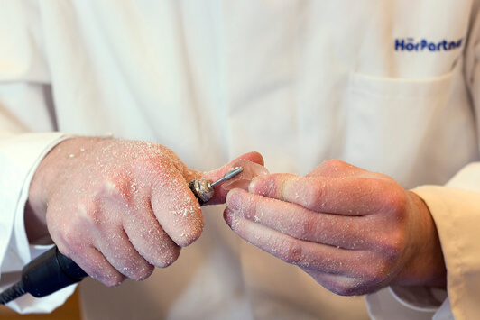 Ein Hörakustiker bearbeitet ein Hörgerät handwerklich mit einem Fräswerkzeug.